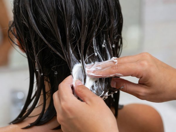 Shallow depth close-up of hands smoothing white conditioning cream onto wet hair ends in sections