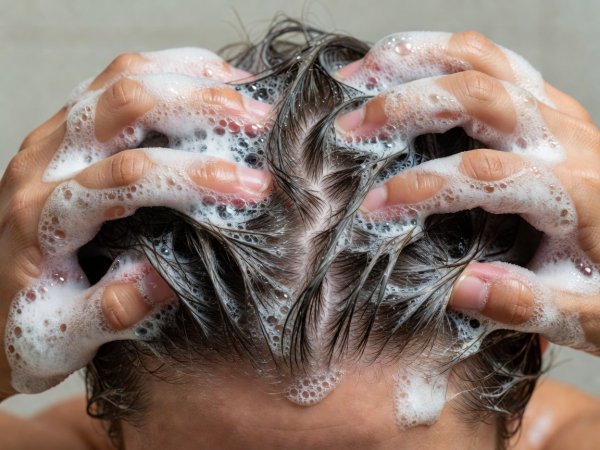 Close-up of fingertips massaging emulsified shampoo foam strictly across the scalp crown