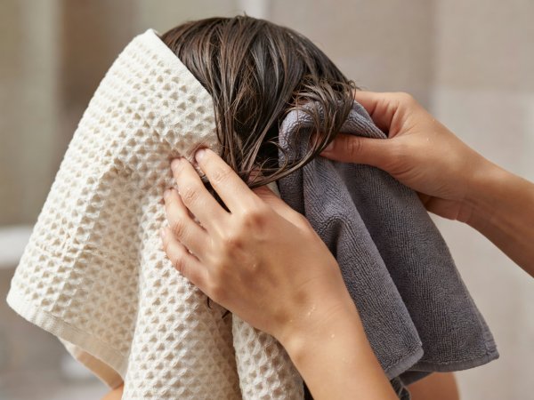 Close-up of hands gently pressing damp hair sections between folds of a waffle-weave towel